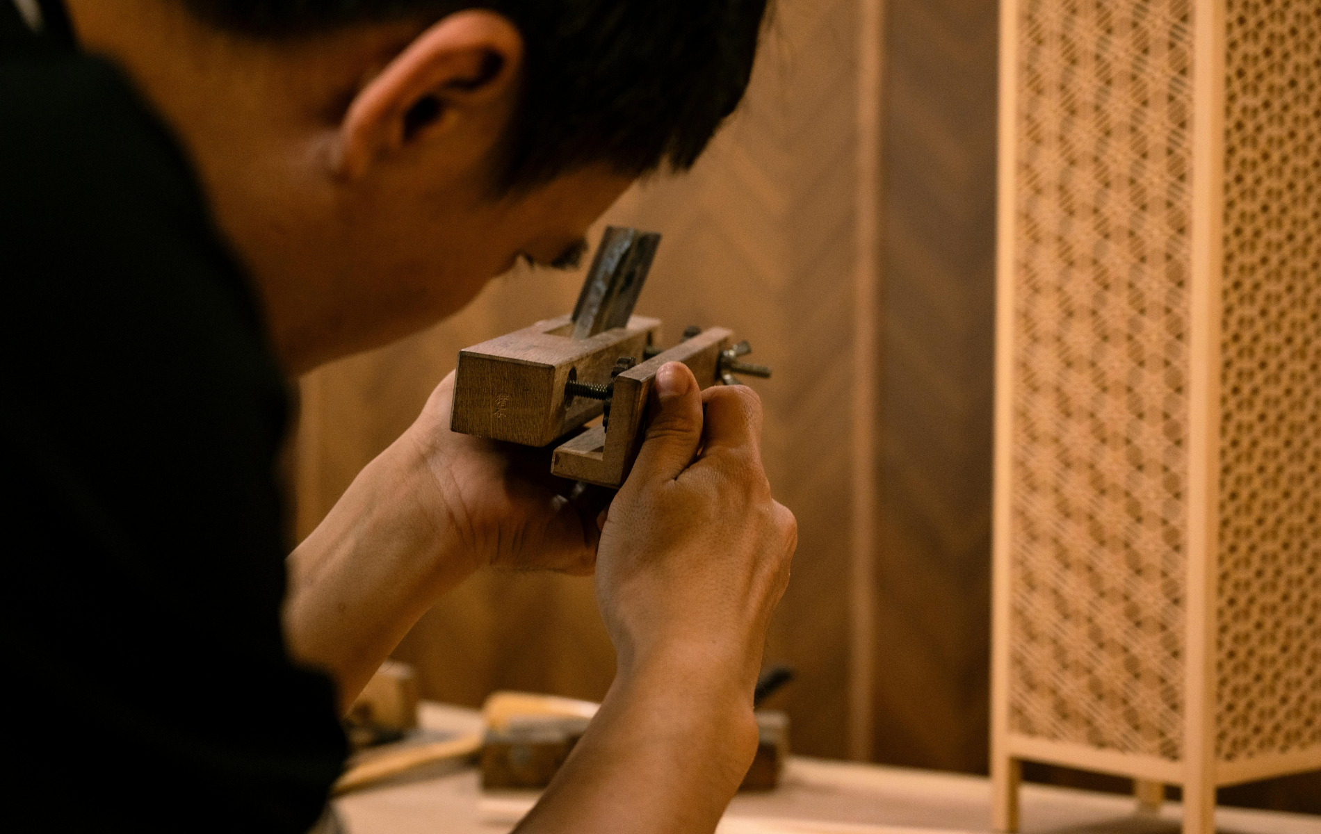 A person focuses on adjusting the metal blade of a small wooden hand plane in a workshop.