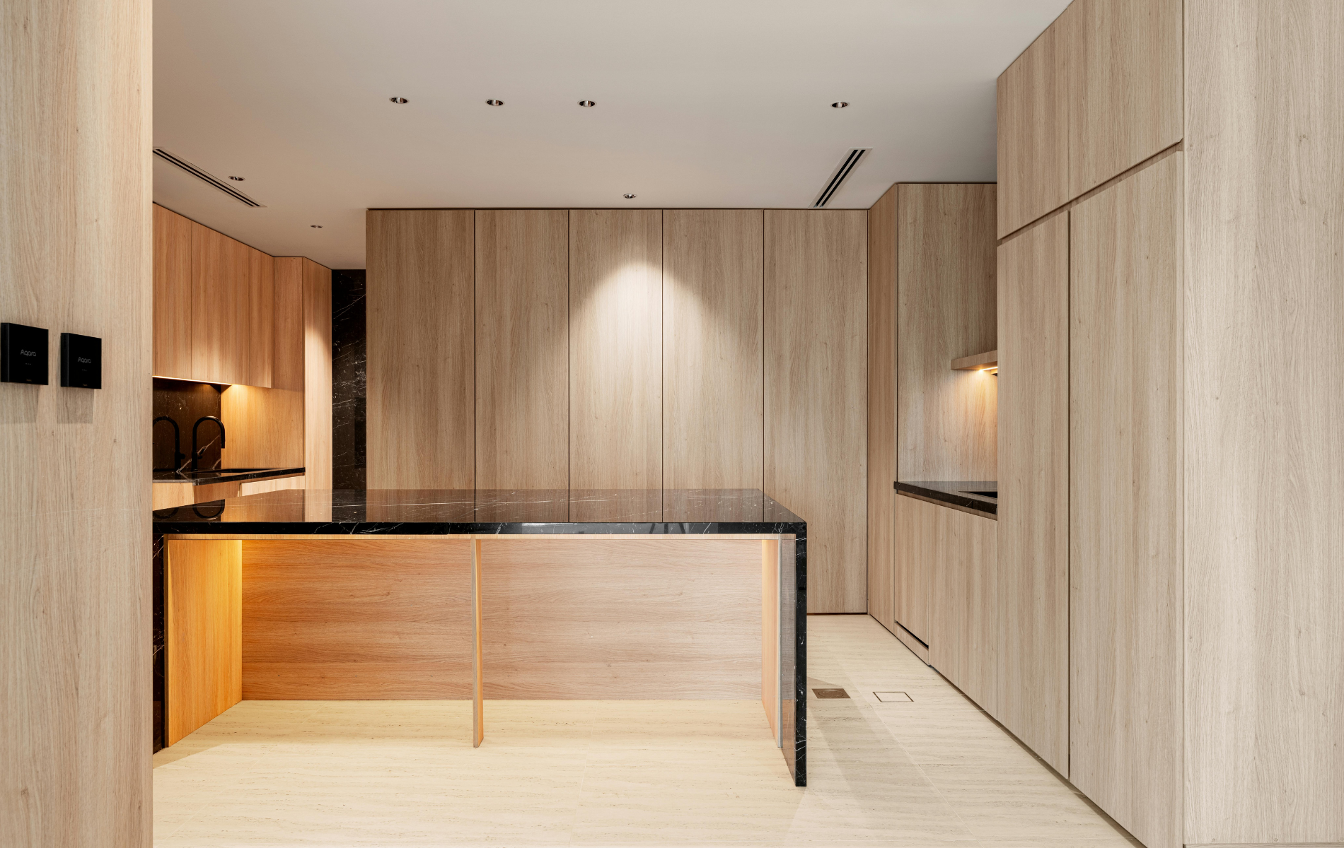 A modern minimalist kitchen with light wood cabinetry, a black stone island, and warm under-cabinet lighting.