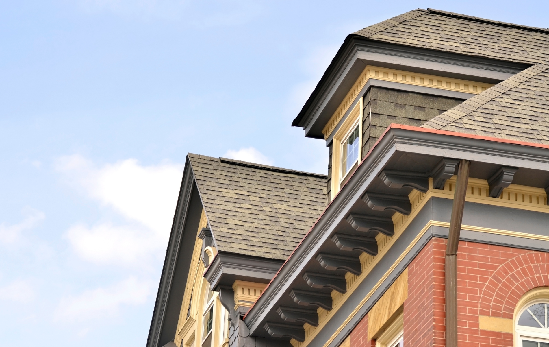 The upper stories and tiled roofline of a red brick building with ornate, dark-colored architectural molding.