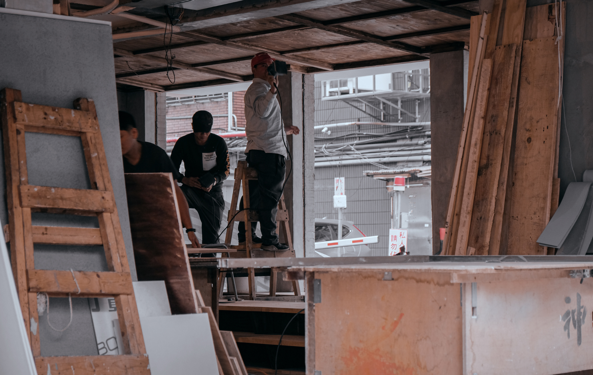 Construction workers stand inside an unfinished building space with wooden panels, tools, and materials around them.