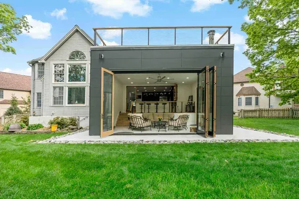 A modern dark-gray backyard structure with folding glass doors, an open-concept interior, and a rooftop deck.