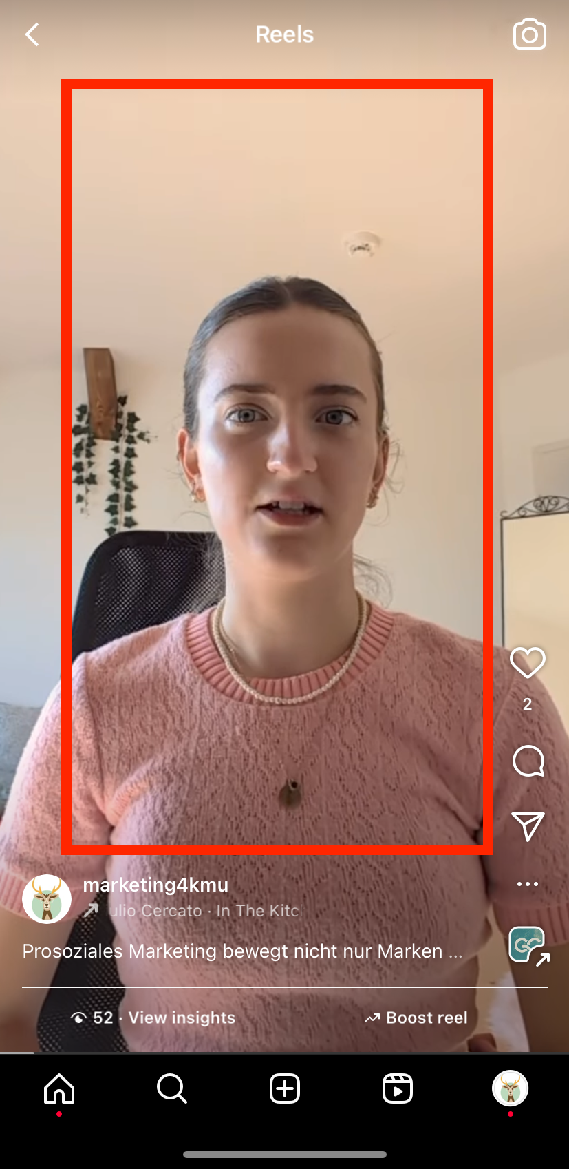 Eine Frau in einem rosa Pullover steht vor einer weißen Wand.