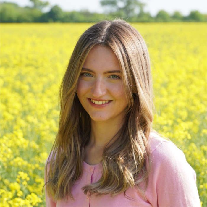 Eine lächelnde Frau in einem rosa Hemd steht in einem gelben Blumenfeld.