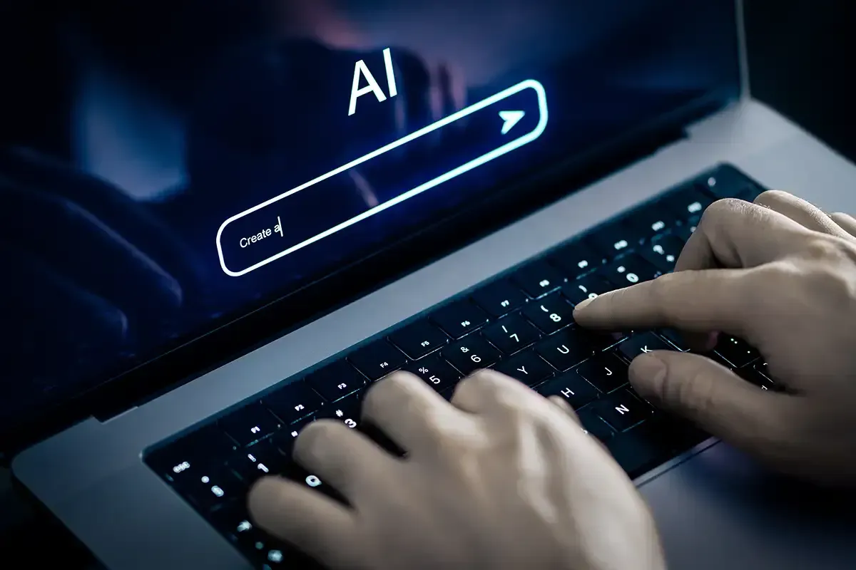 Hände tippen auf einem Laptop, auf dessen Bildschirm das Wort „KI“ zu sehen ist.