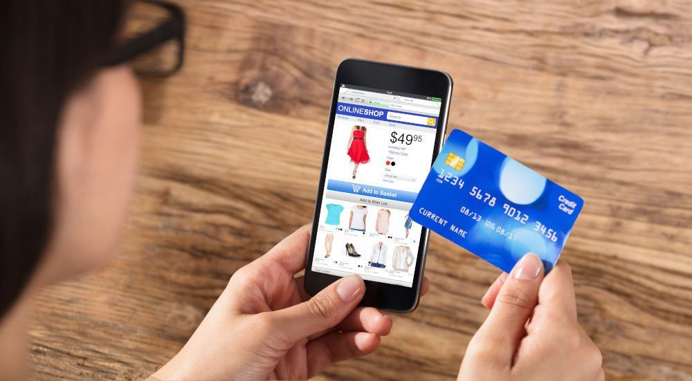Eine Person hält eine Kreditkarte und ein Smartphone in der Hand und kauft online Kleidung ein.