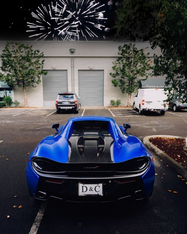 Blue sports car parked in front of a garage at night, with fireworks above.