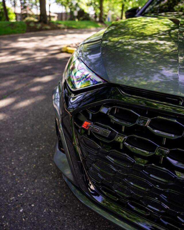 Close-up of a black car’s front grille and headlight on a sunlit road