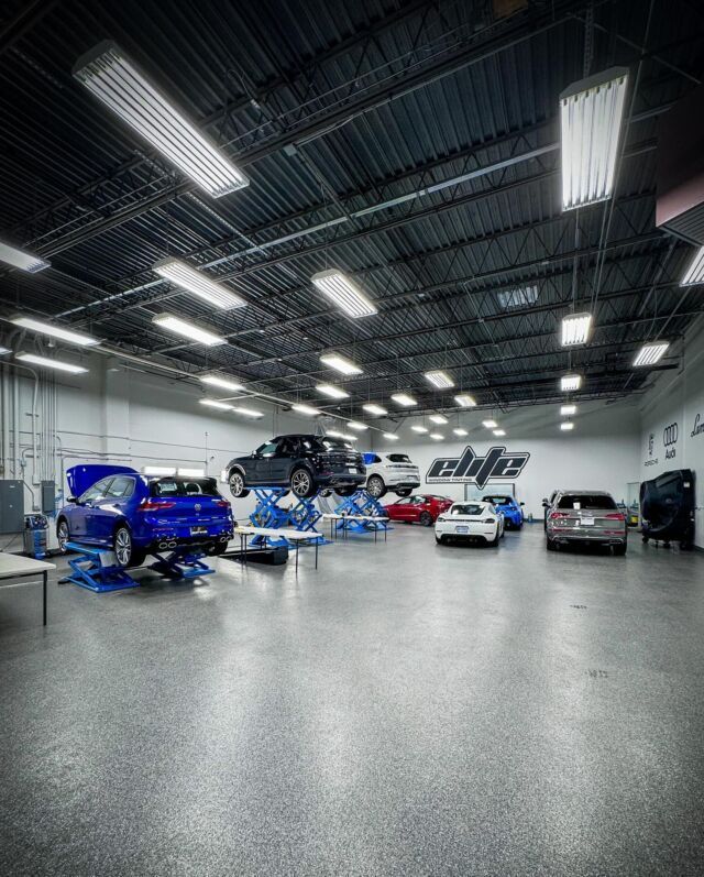 Car shop interior with multiple cars under bright ceiling lights, including a blue car on a lift.