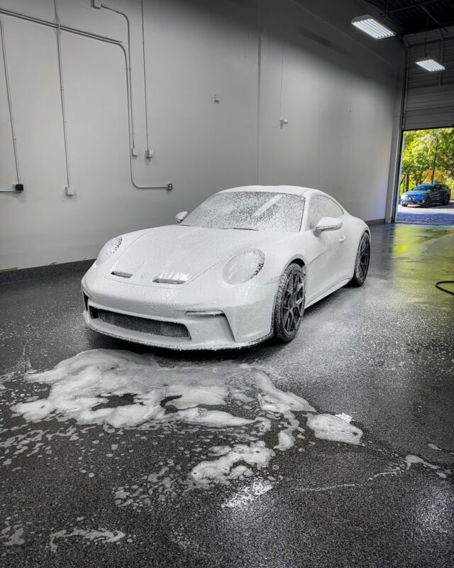 White sports car covered in foam in an indoor car wash bay