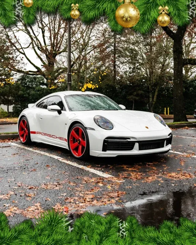 White Porsche sports car with red wheels parked on a wet road with autumn leaves and trees in the background