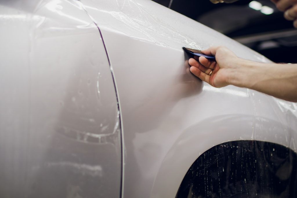 Hand washing a white car with a sponge, water dripping over the side.
