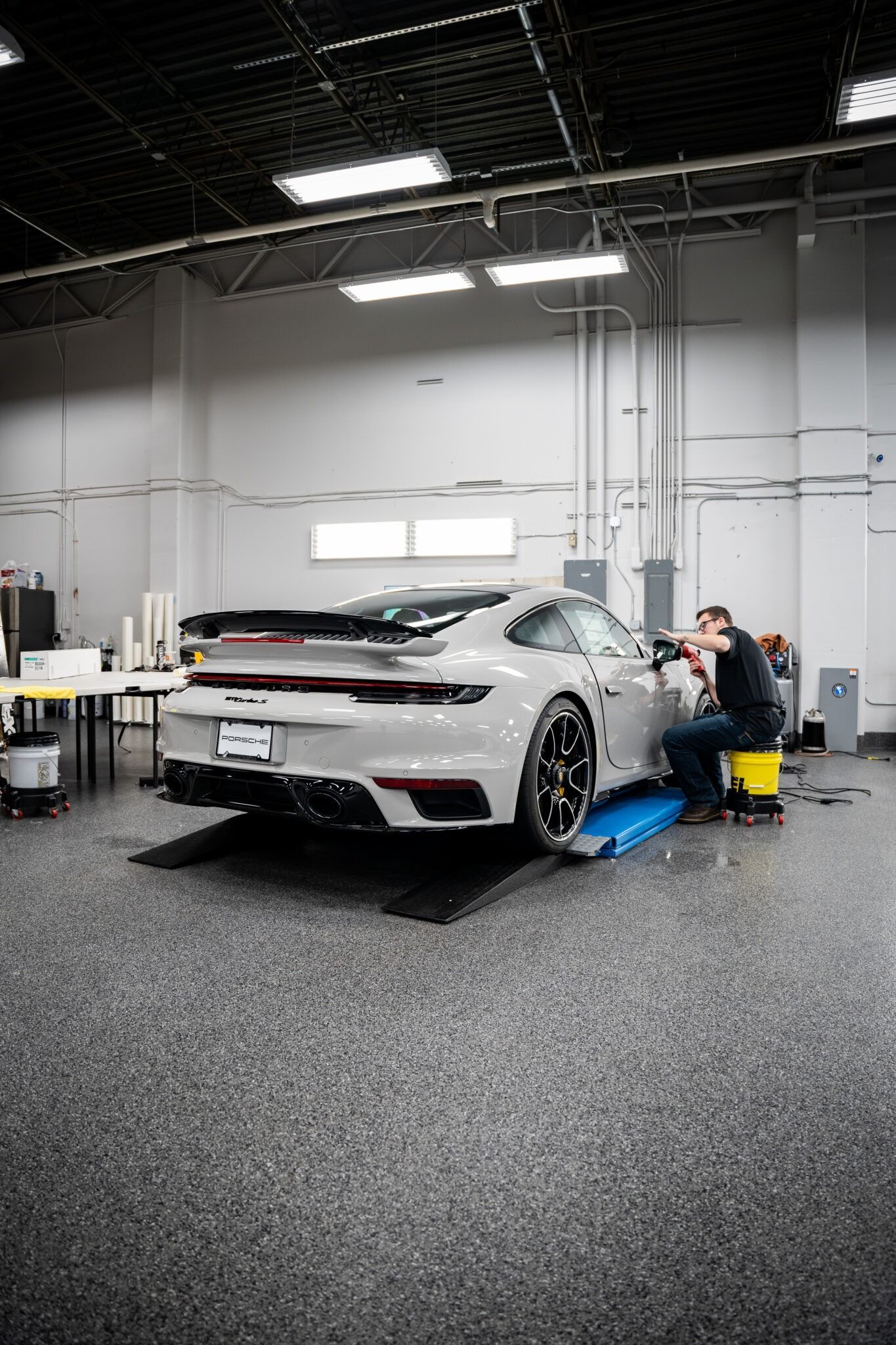 White sports car being detailed in a workshop, with a person working beside it