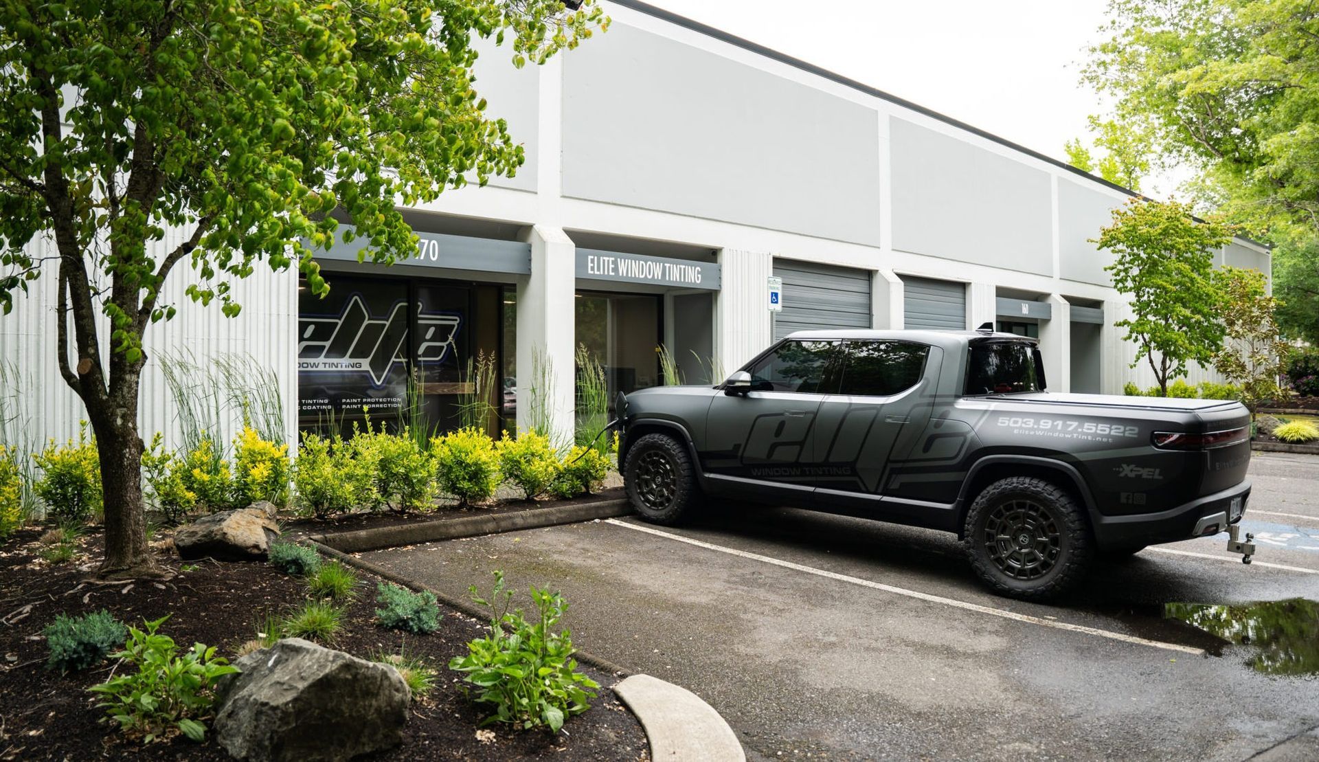 Black pickup truck parked in front of a modern white building with a curved driveway and greenery