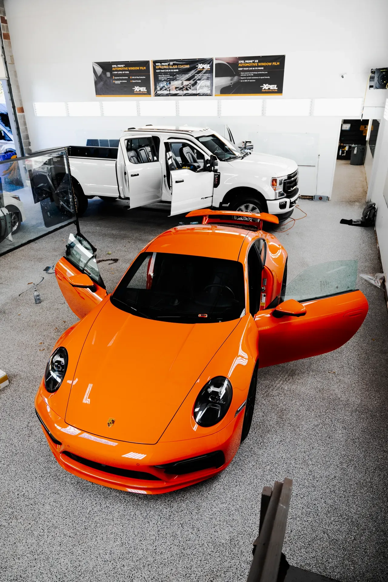 Orange sports car with doors open in a showroom, with a white car and wall displays behind it