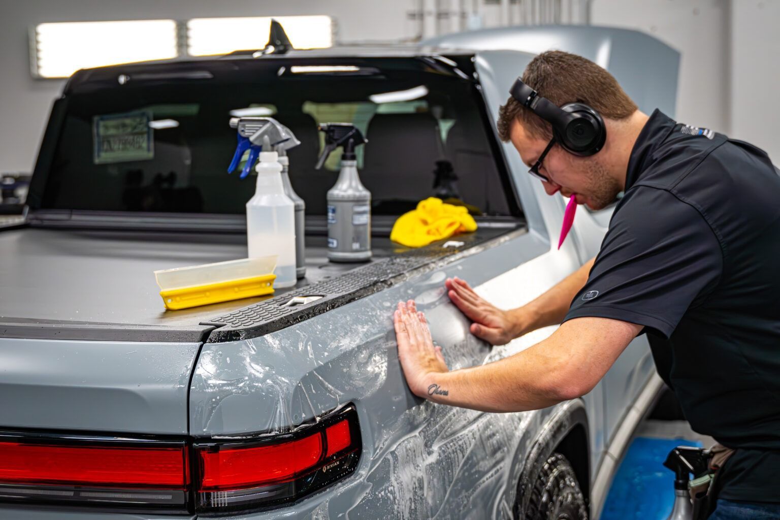 Detailing technician polishing a silver car in a garage, with spray bottles and cloths nearby