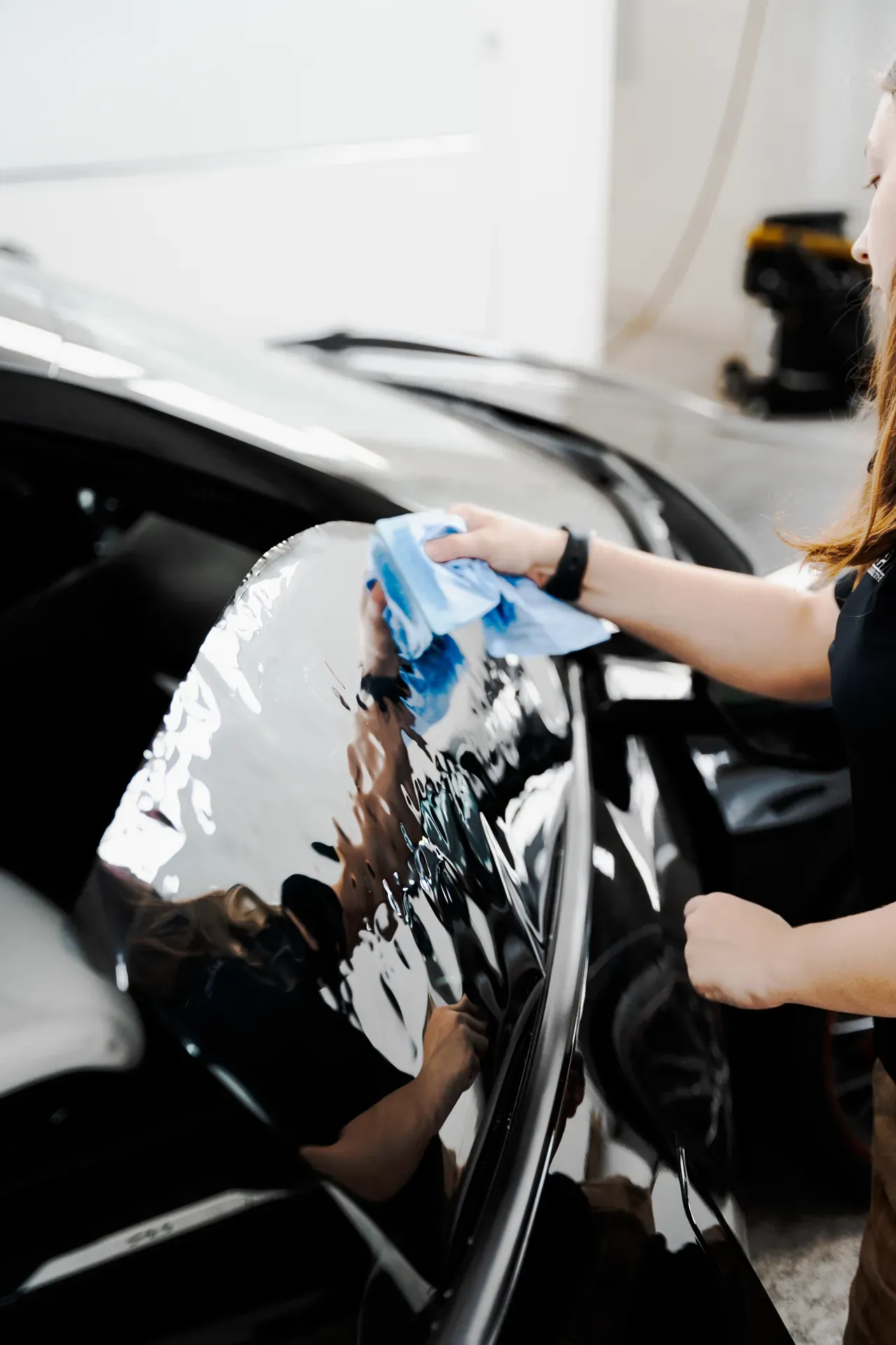 Person wiping a black car with a blue cloth in a garage