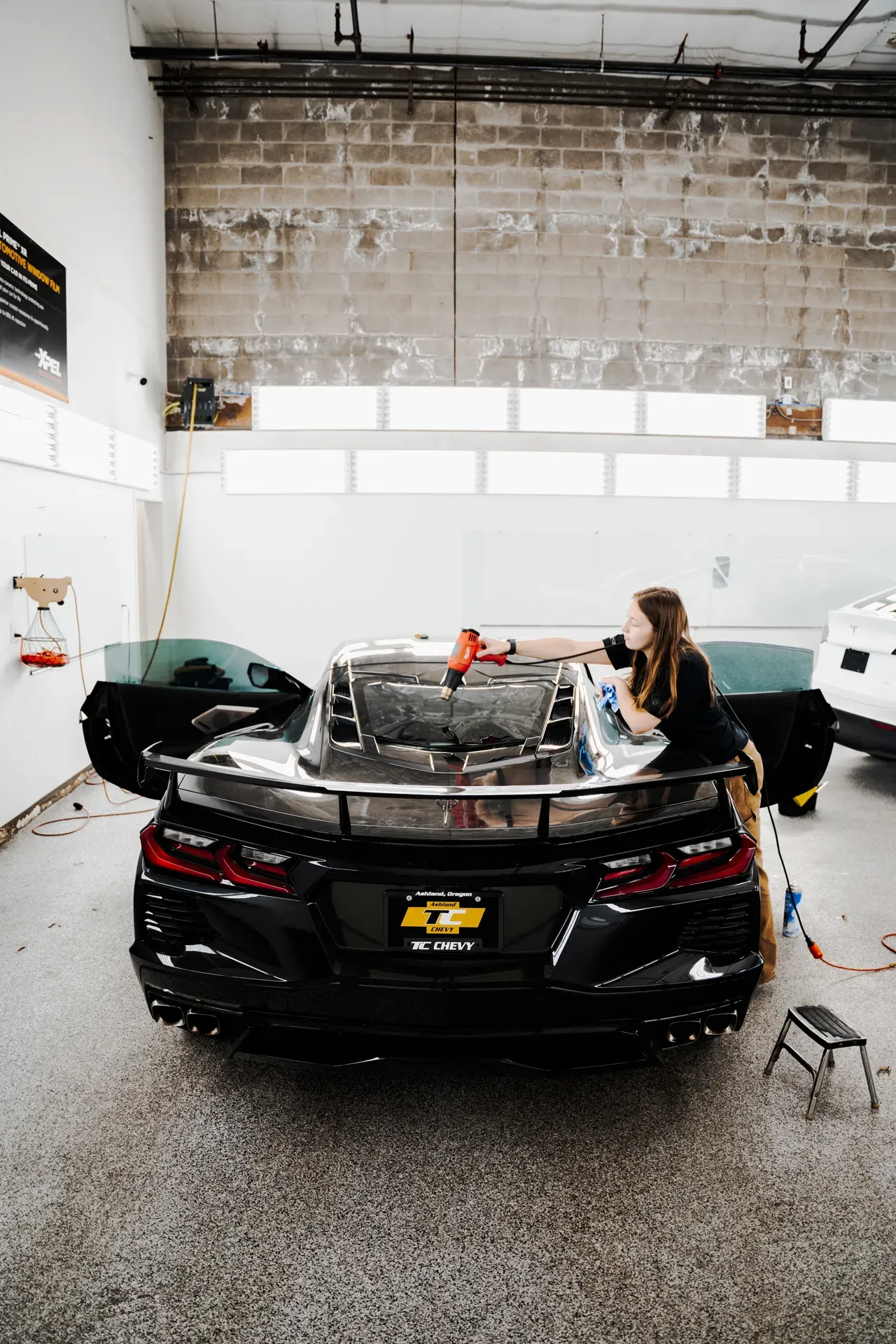 Black sports car in a garage, with a person working on the open rear trunk area.