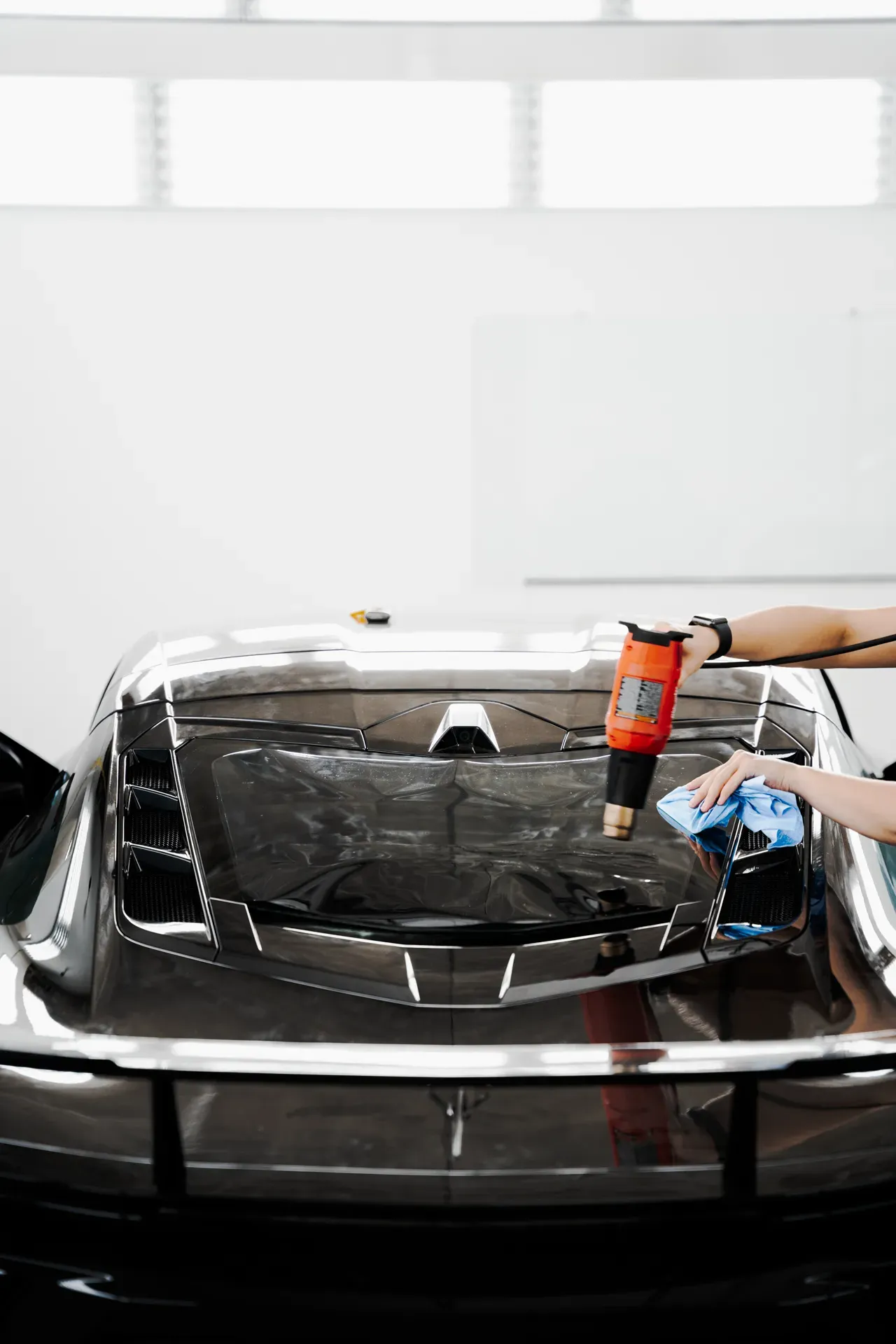 Person polishing a black classic car in a bright garage with a buffer tool