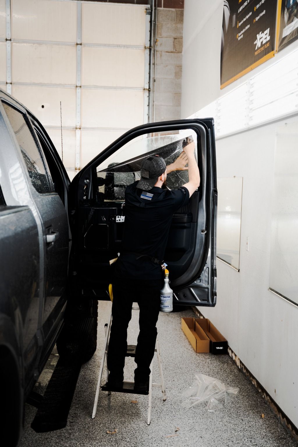 Person in dark clothing entering a black vehicle in a garage, with the driver’s door open.