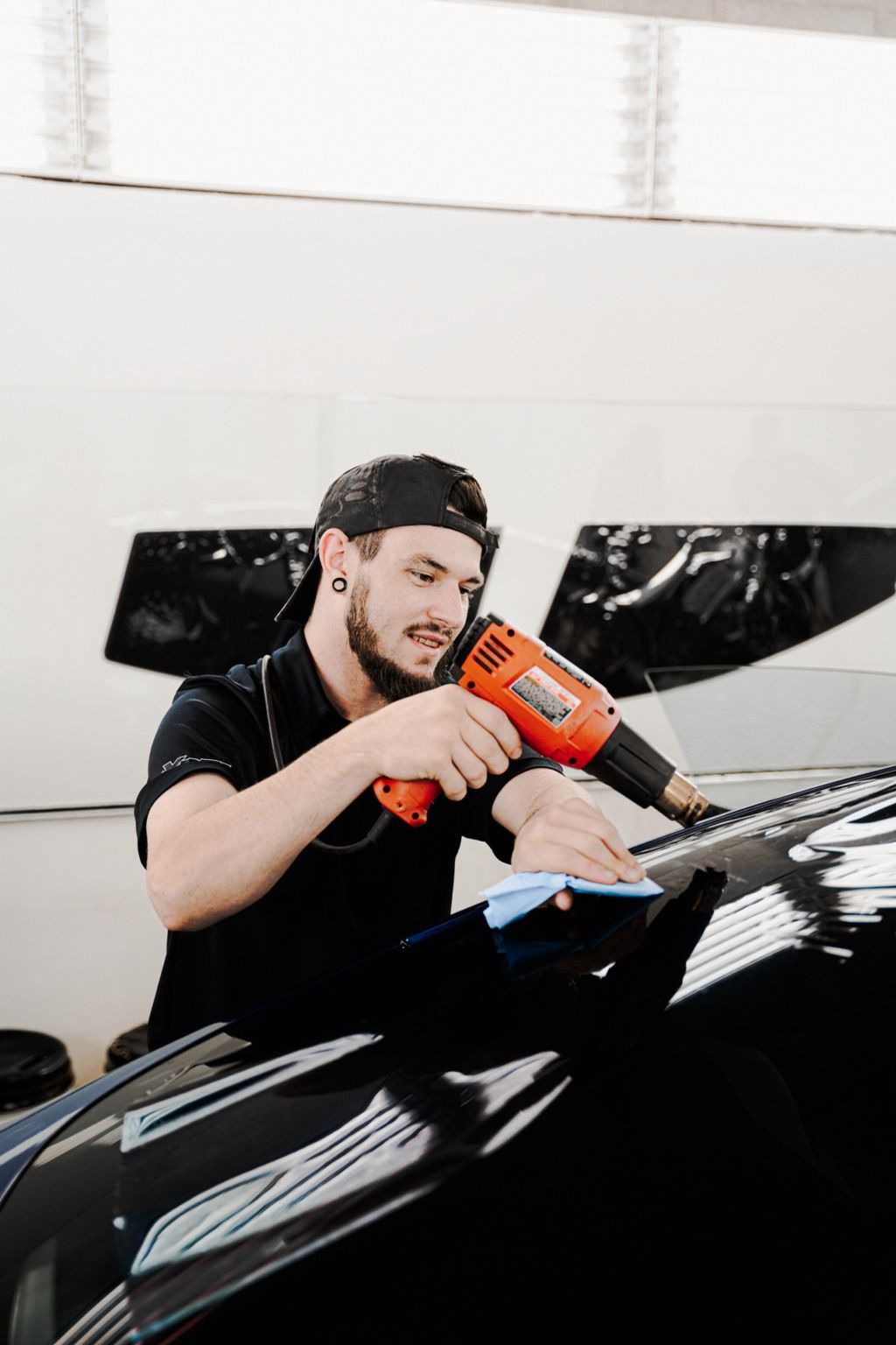 Mechanic using an orange drill on a glossy black car in a bright garage