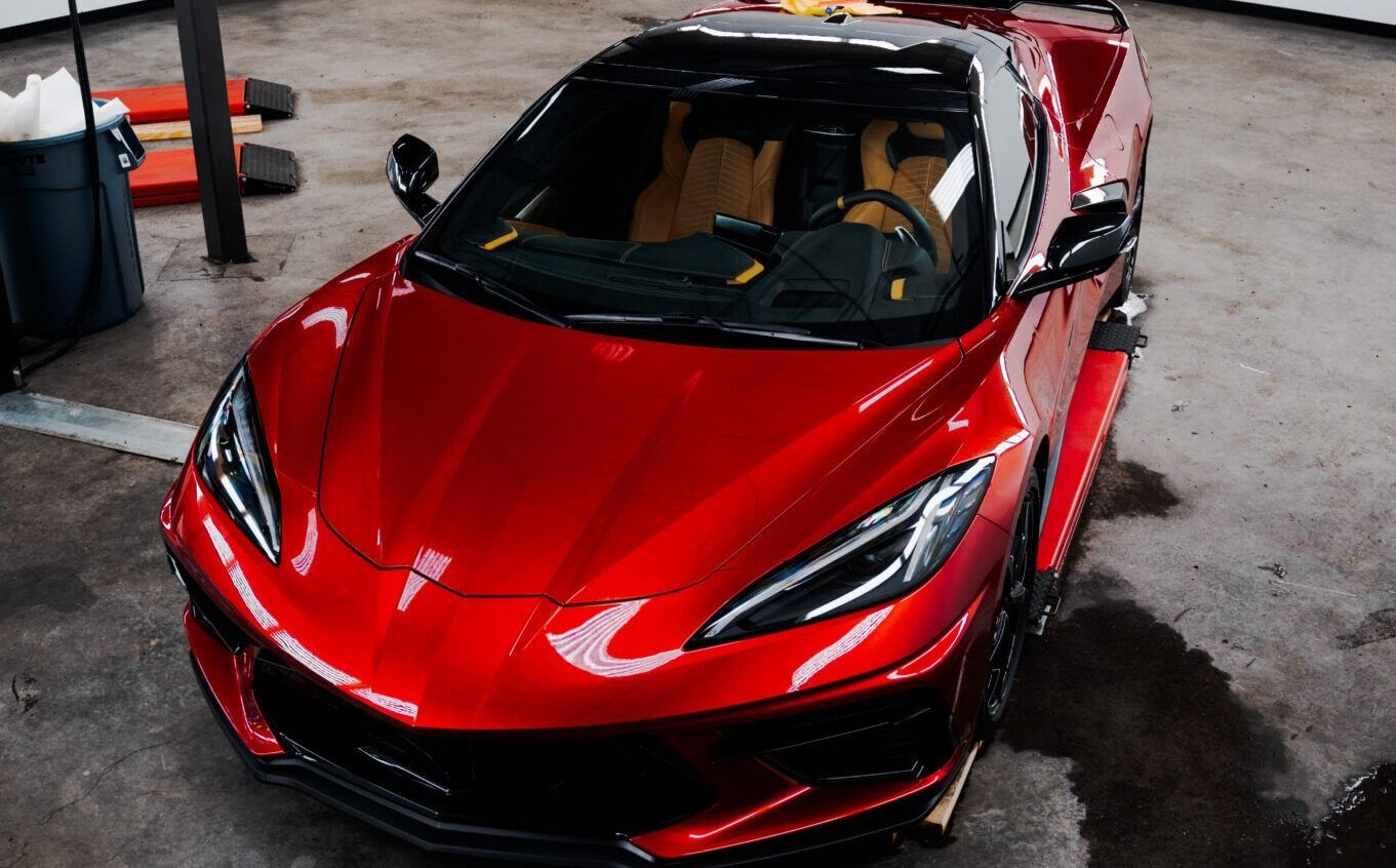 Red sports car parked indoors, viewed from the front in a garage-like setting.