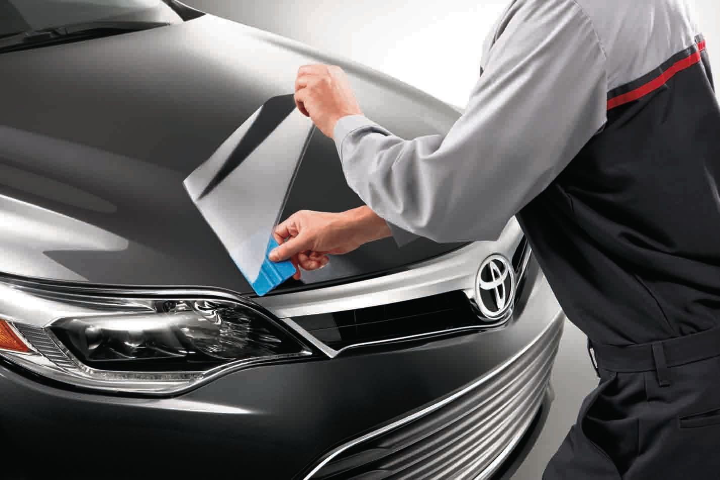 Worker applying protective film to the front hood of a black car