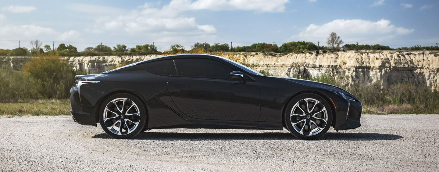 Black sports coupe parked on gravel with a rocky embankment in the background