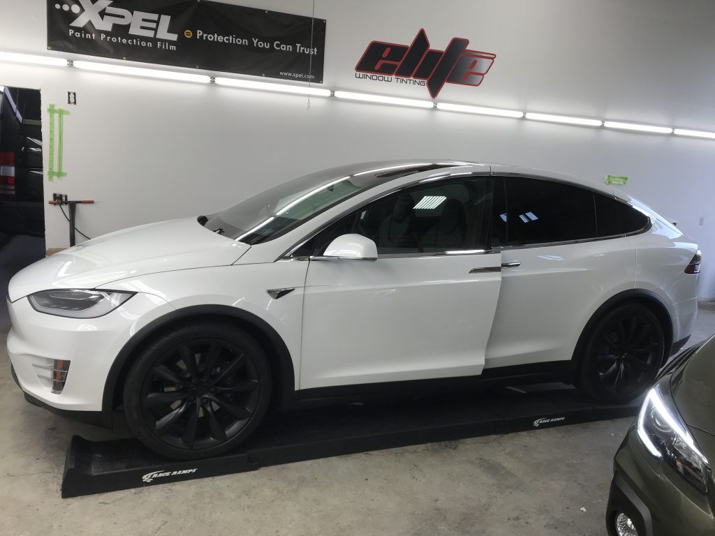 White Tesla Model X parked indoors in a garage, with black wheels and a black roof.