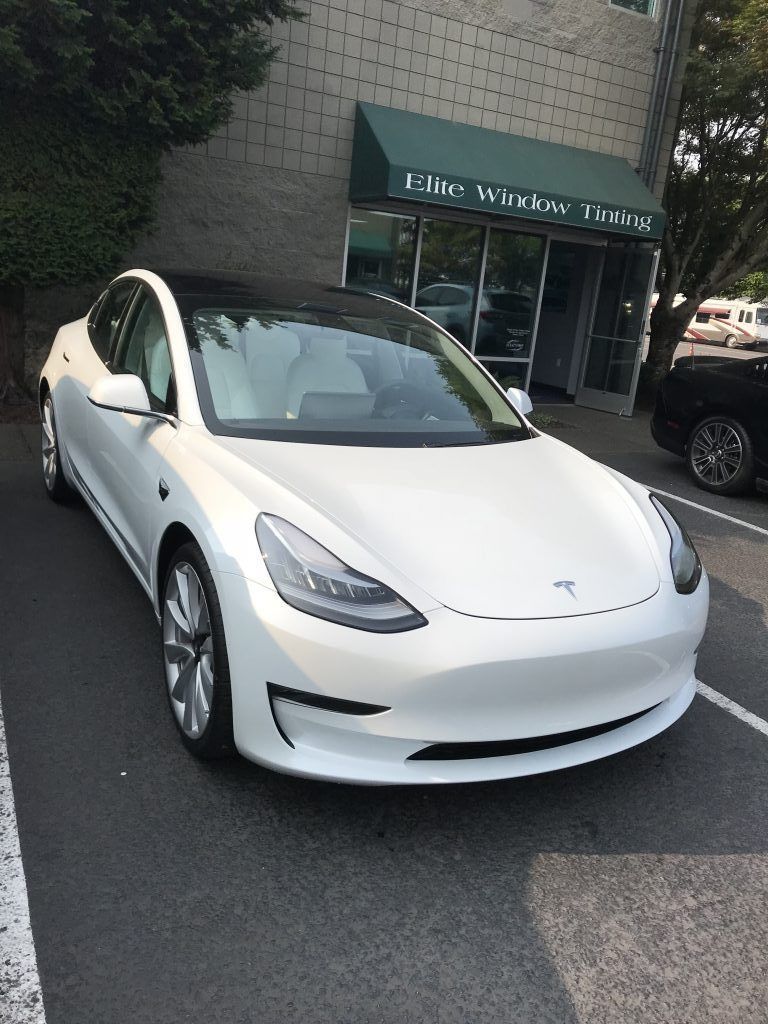 White Tesla parked outside a building with a green awning and trees nearby