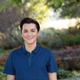 Person in a blue polo shirt smiling outdoors with a blurred garden background