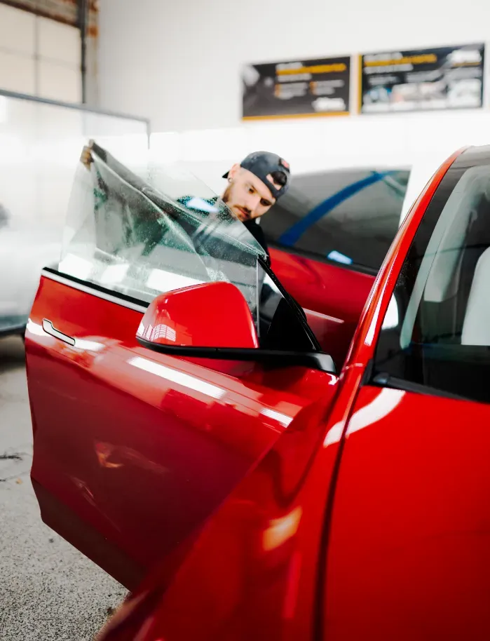 Person cleaning a red car window in a garage