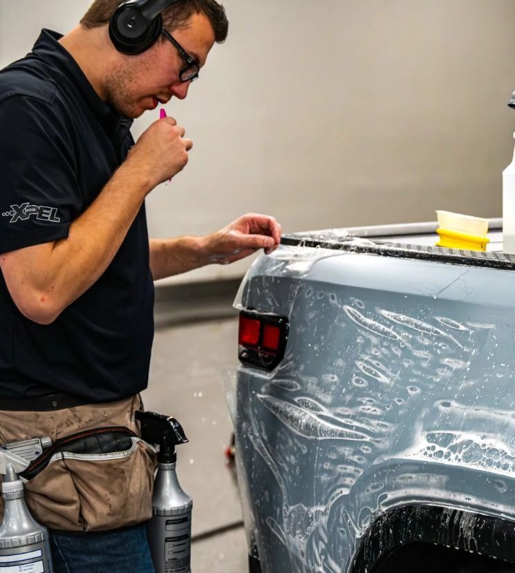 Man polishing a silver car panel with headphones on in a garage