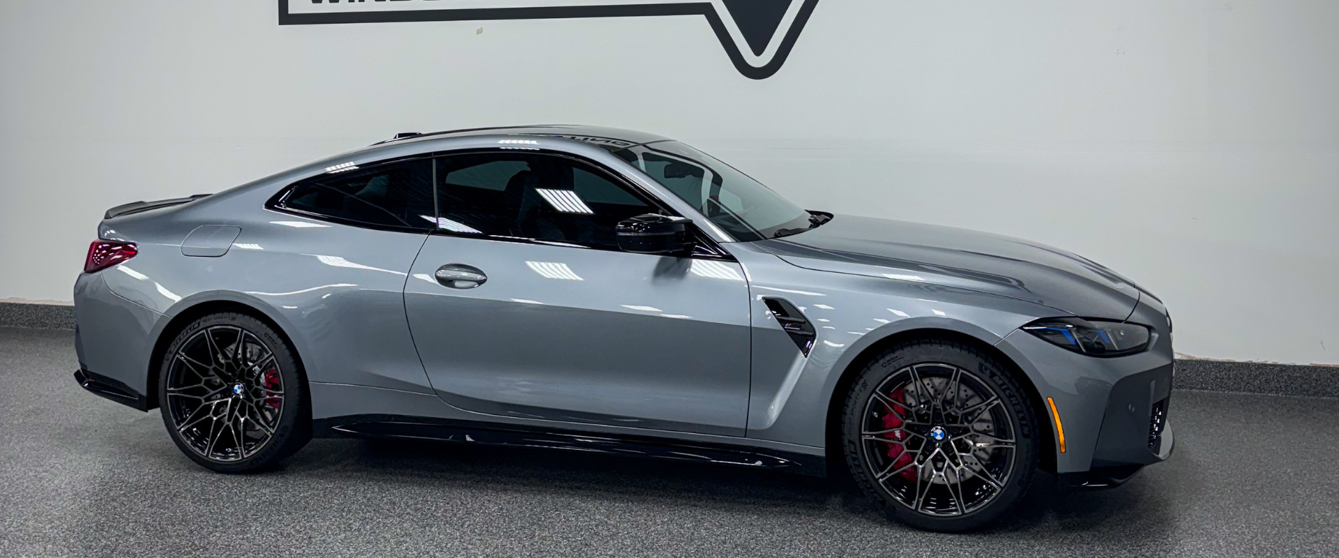 Silver sports coupe in side profile, with black wheels and red brake calipers, on a showroom floor