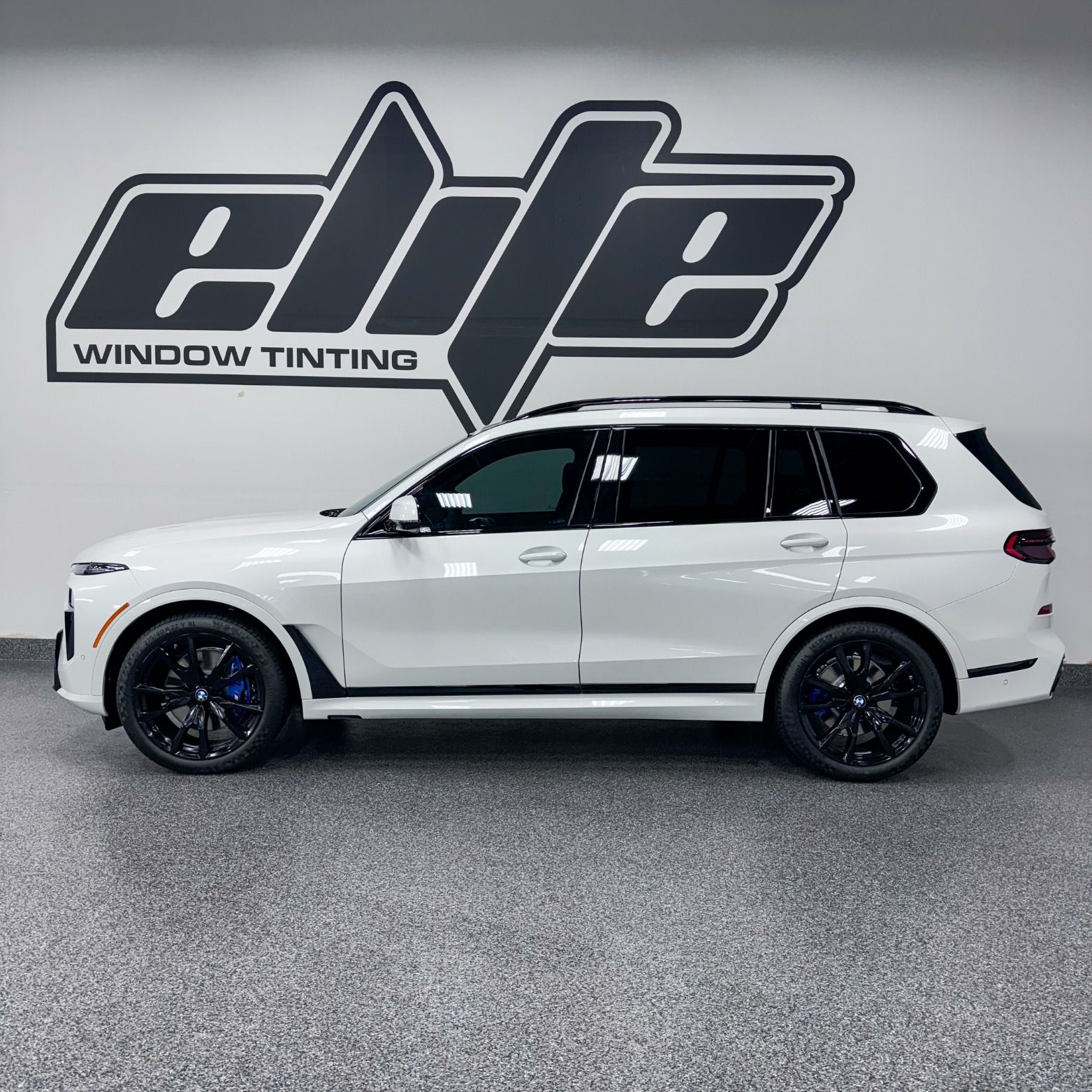 White SUV with black wheels parked indoors in front of an elite window tinting wall logo