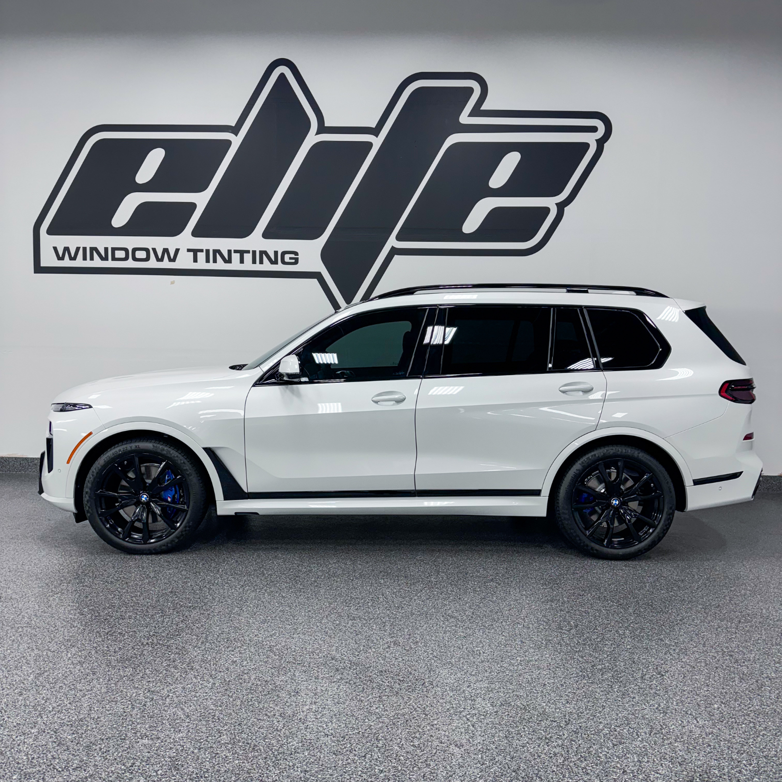 White SUV in a window tinting shop, parked in front of an “elite” wall logo.