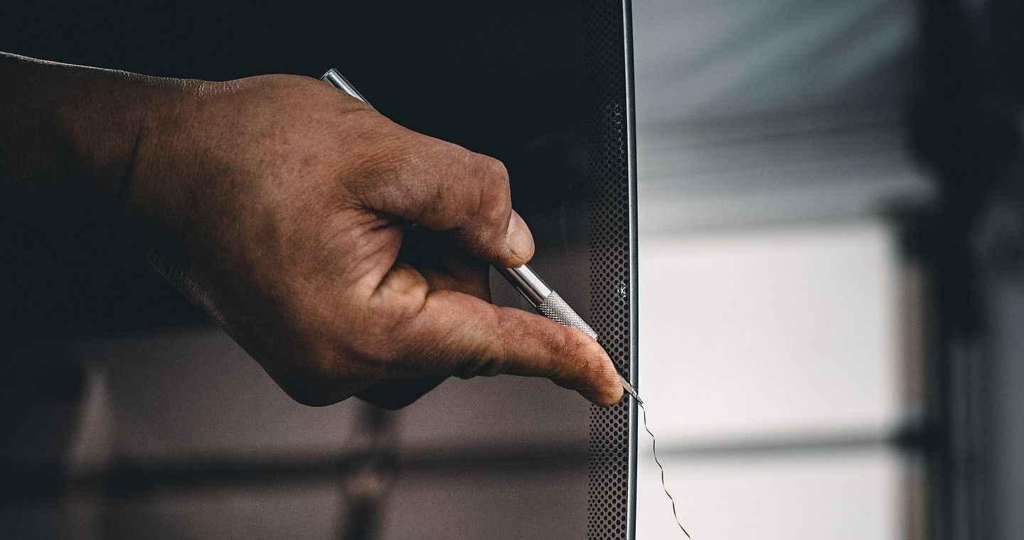 Hand holding a pen near a textured glass panel, marking or drawing a line along the edge.