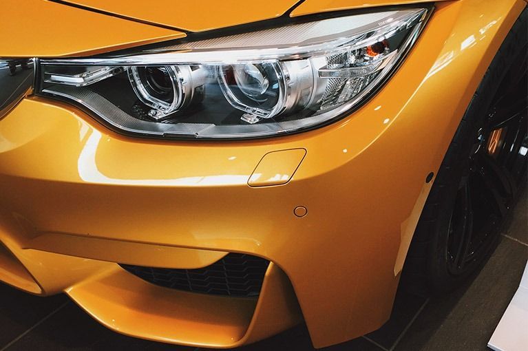 Close-up of a bright orange sports car’s front headlight and bumper