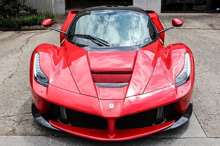 Red sports car parked on pavement, front view, with sleek aerodynamic body and black roof.