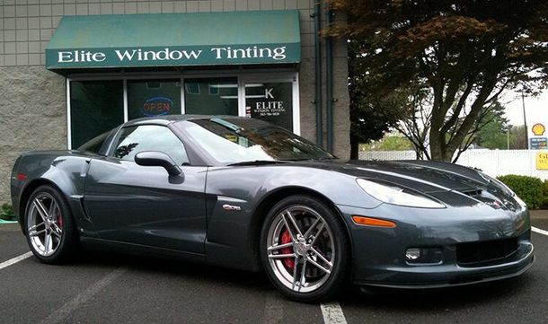 Gray sports car parked outside Elite Window Tinting storefront, with trees and sidewalk in the background.
