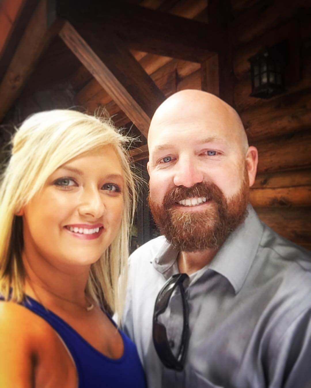 Two smiling people posing indoors, with wood beams in the background.
