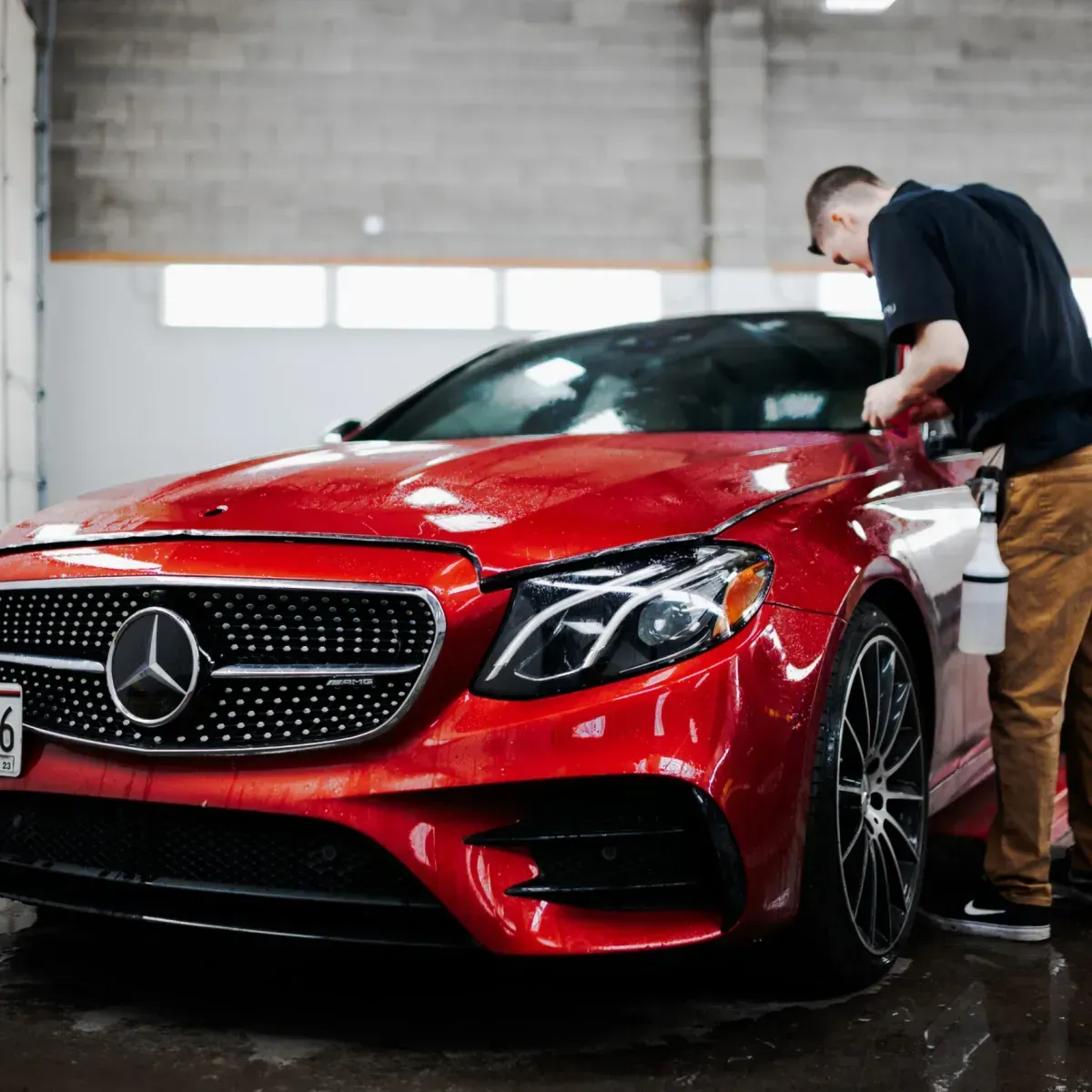 Red Mercedes sports car being cleaned by a person in a garage