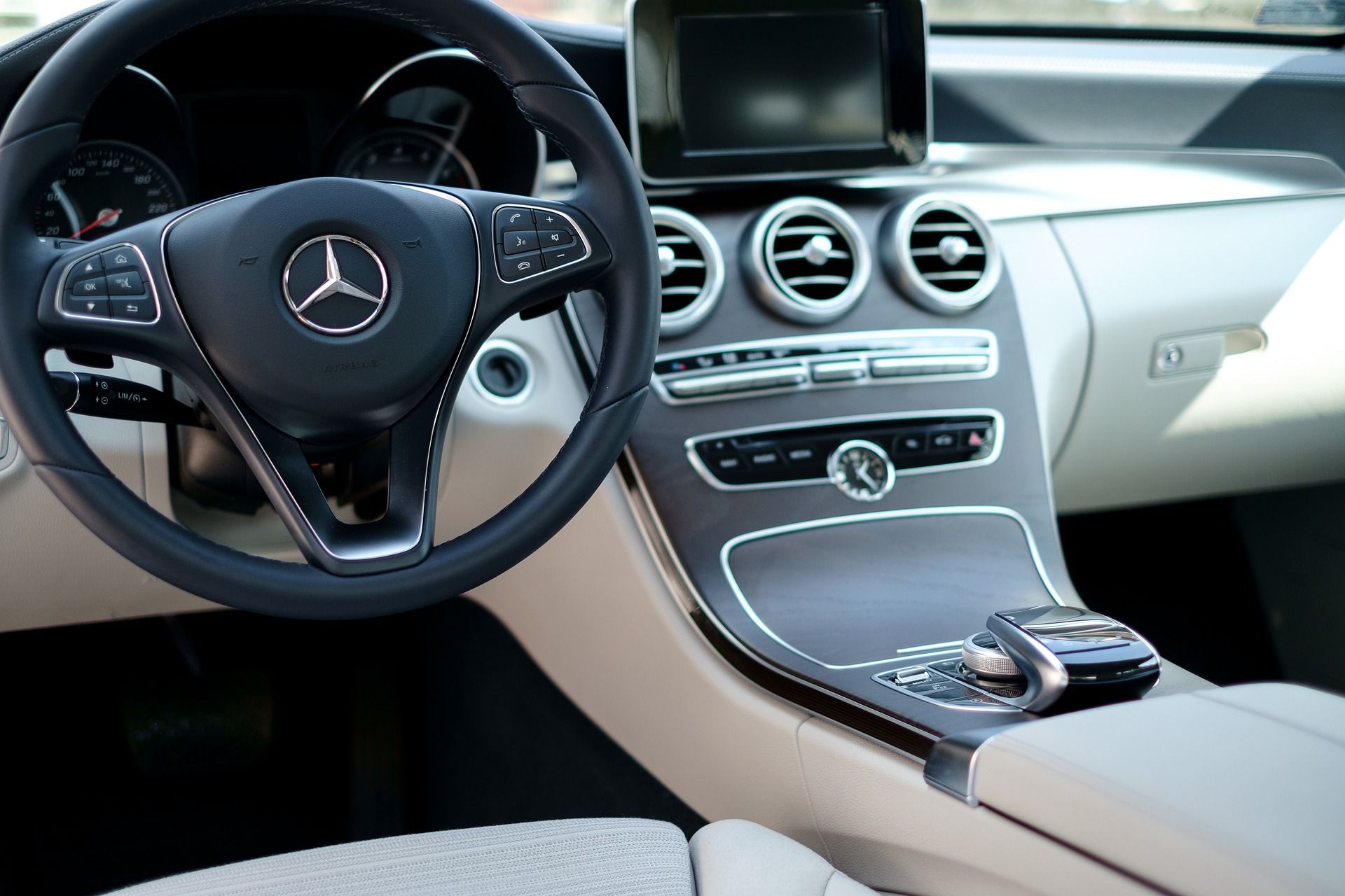 Luxury car interior with Mercedes steering wheel, circular vents, and black-and-beige dashboard and center console
