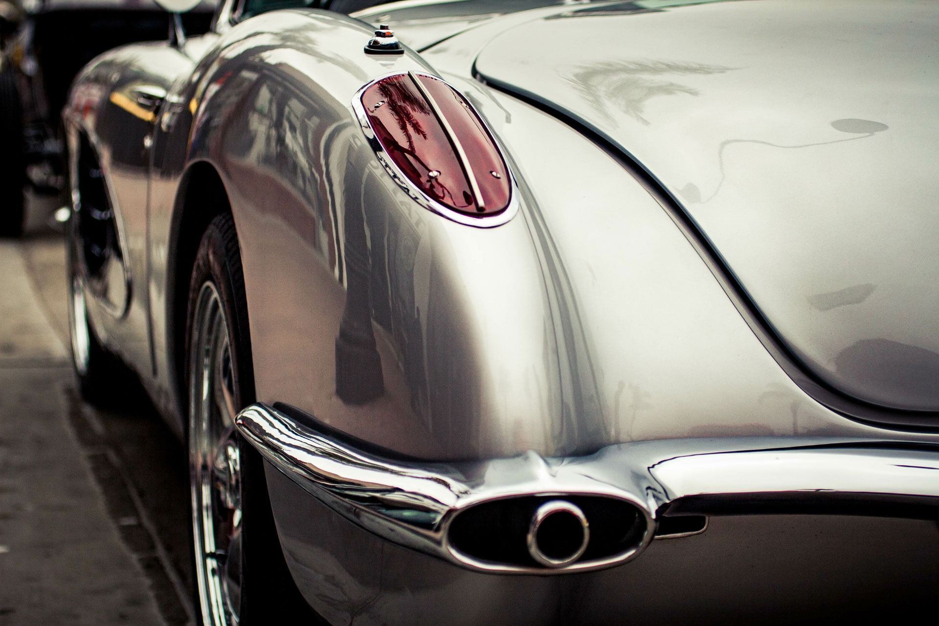 Rear view of a silver vintage sports car with chrome details and red taillights