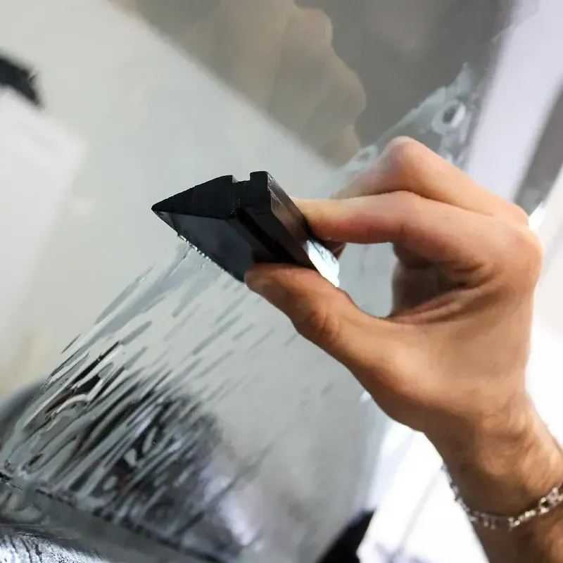 Hand using a black squeegee to apply or smooth a tinted film on glass