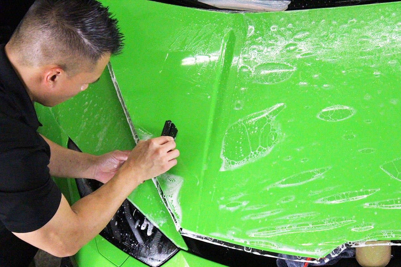 Person peeling clear film from a bright green car panel with a black vent area.