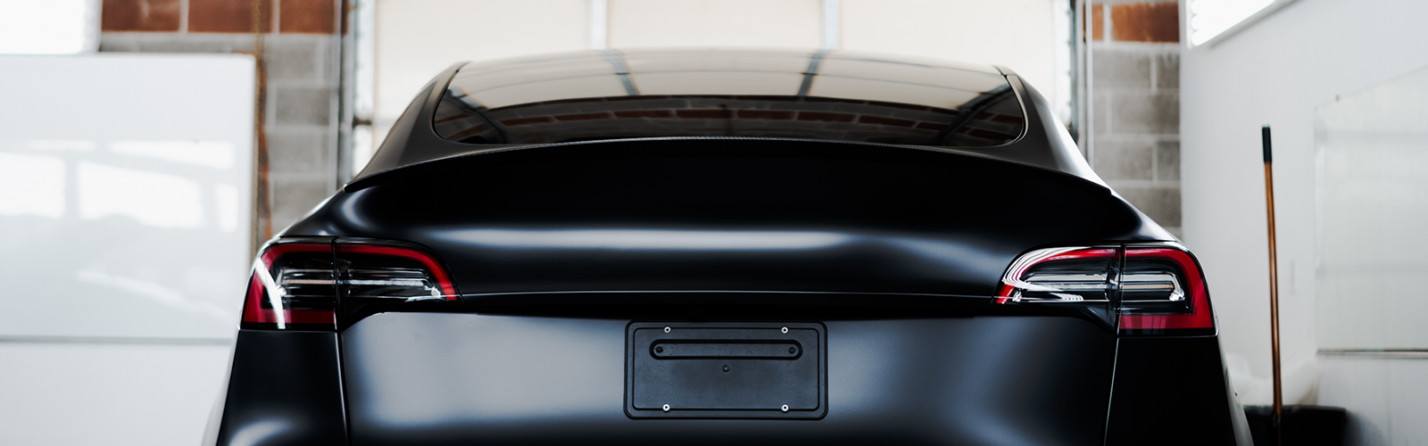 Rear view of a black car parked indoors, with taillights visible in a garage-like space
