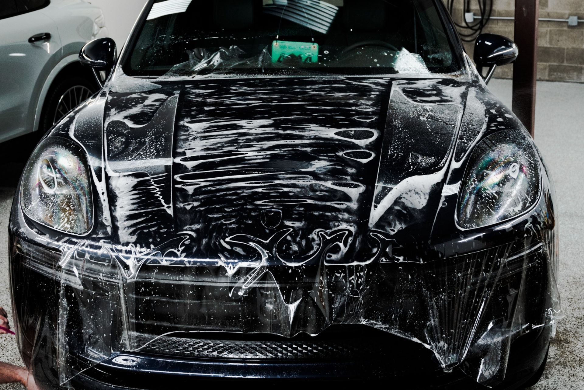 Black sports car being washed in a car wash, covered in white soap suds