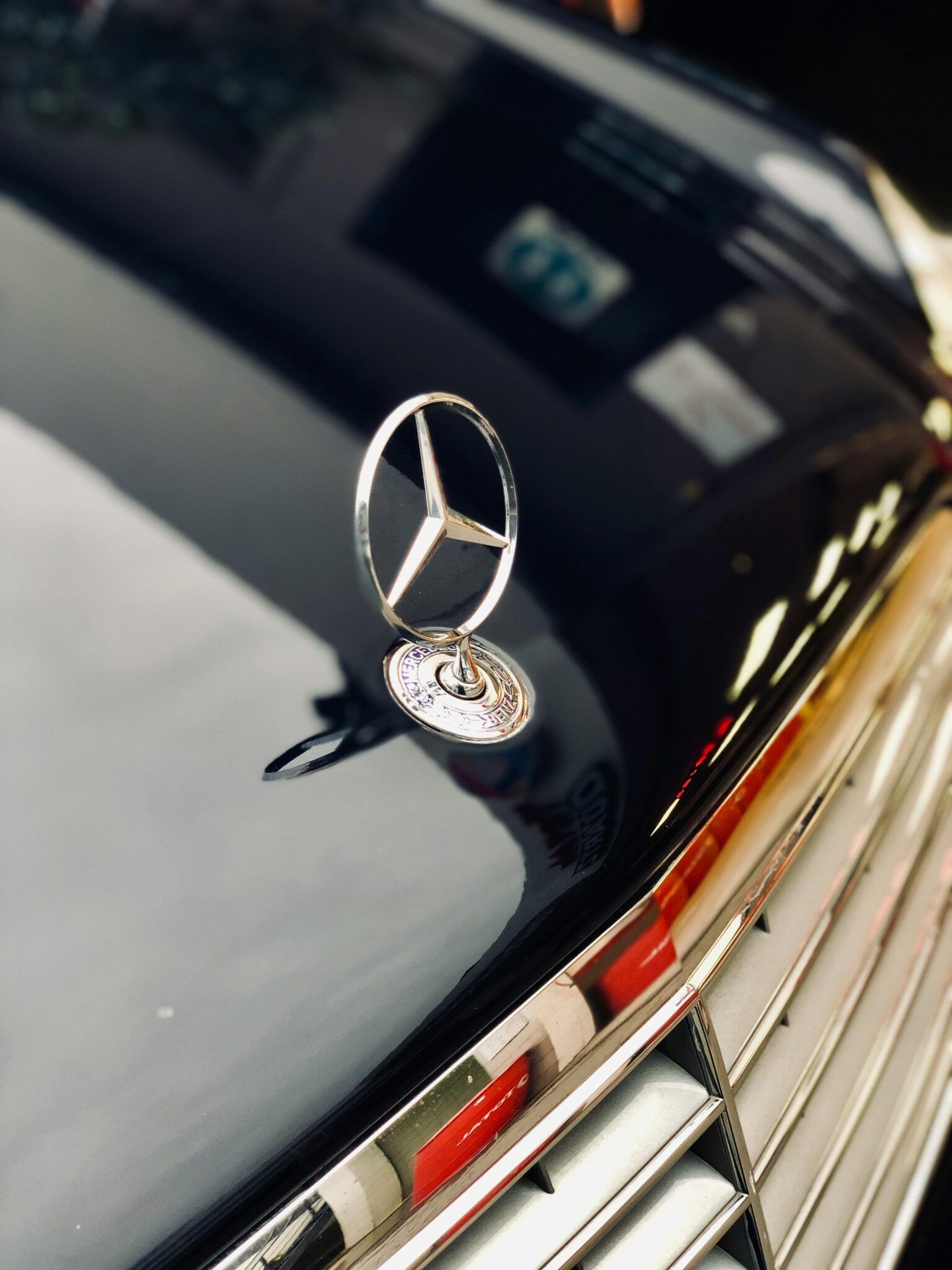 Mercedes-Benz hood ornament on a black car with a chrome grille and red emblem.
