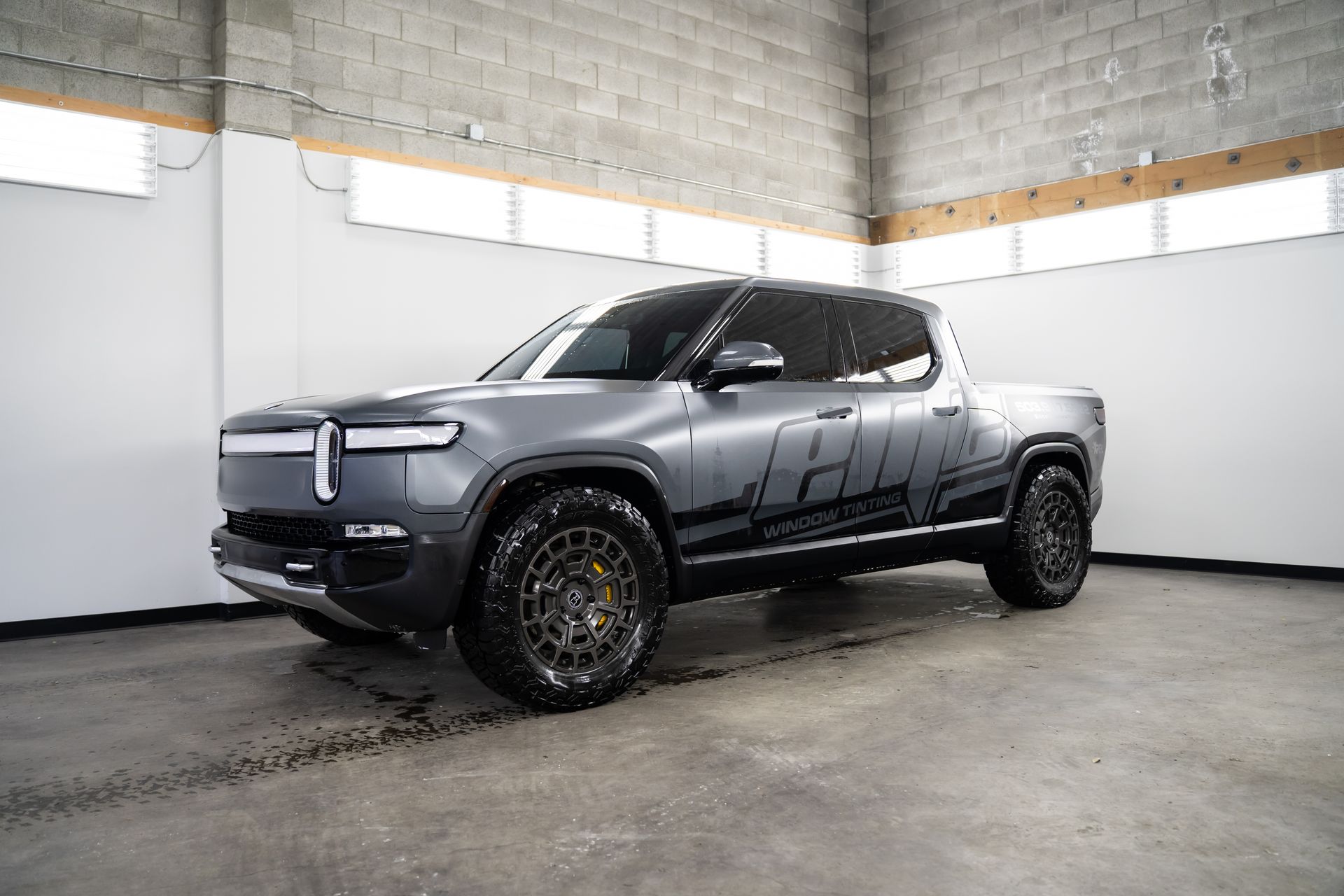 Gray pickup truck in a garage showroom, angled front-left view, with black wheels and tinted windows