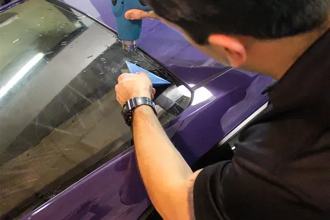 Person applying film to a purple car window with a tool